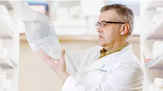 A man in a white coat in a pharmacy looks at a solutions bag