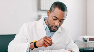 A man in a white coat repairs a medical device placed on a table