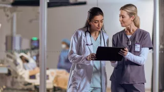 Two female healthcare workers look at data on an tablet 