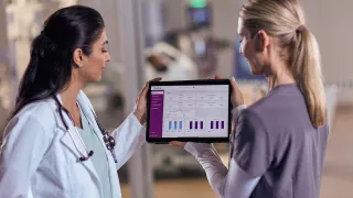 Two female healthcare professionals look at data on an tablet