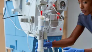 A healthcare professional holds a Theranova dialyzer by a AK 98 machine