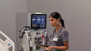 Healthcare professional at the patient bedside in front of the PrisMax System