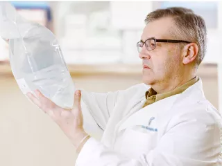 A man in a white coat in a pharmacy looks at a solutions bag