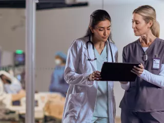 Two female healthcare workers look at data on an tablet 