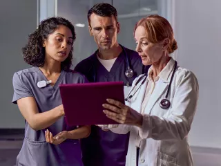 Three healthcare professionals gather round a tablet to review data