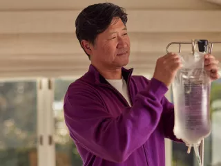 A man in his living room hangs up his bag of Dianeal peritoneal dialysis (PD) solution