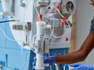 A healthcare professional holds a Theranova dialyzer by a AK 98 machine
