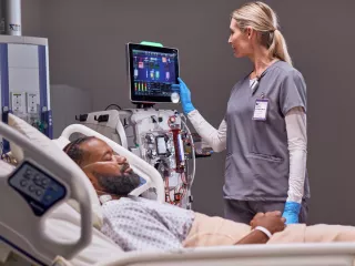 A healthcare professional at the patient's bedside working with the PrisMax system